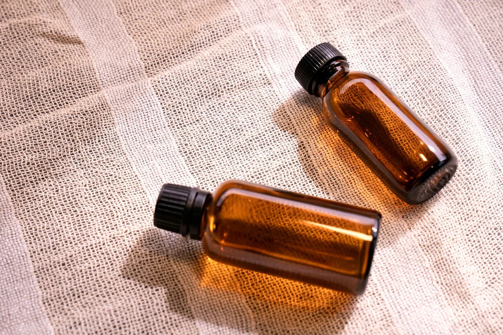 Deux petits flacons en verre ambré posés sur un tissu de lin clair