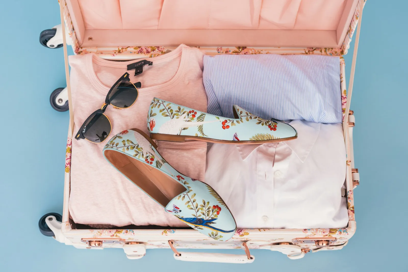 Valise rose ouverte avec vêtements pliés, chaussures et lunettes de soleil