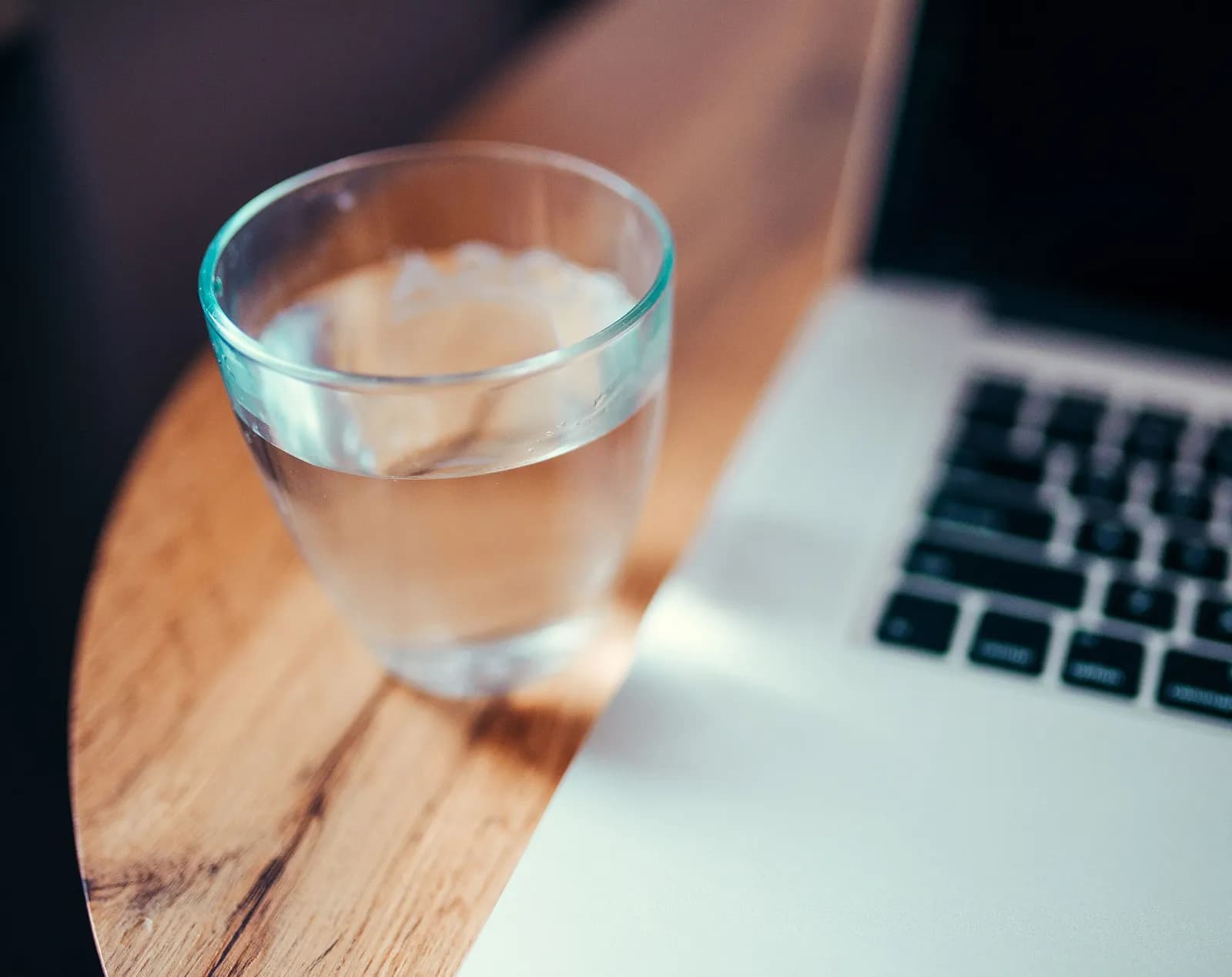 Verre d'eau posé sur une table en bois, au bord d'un ordinateur portable