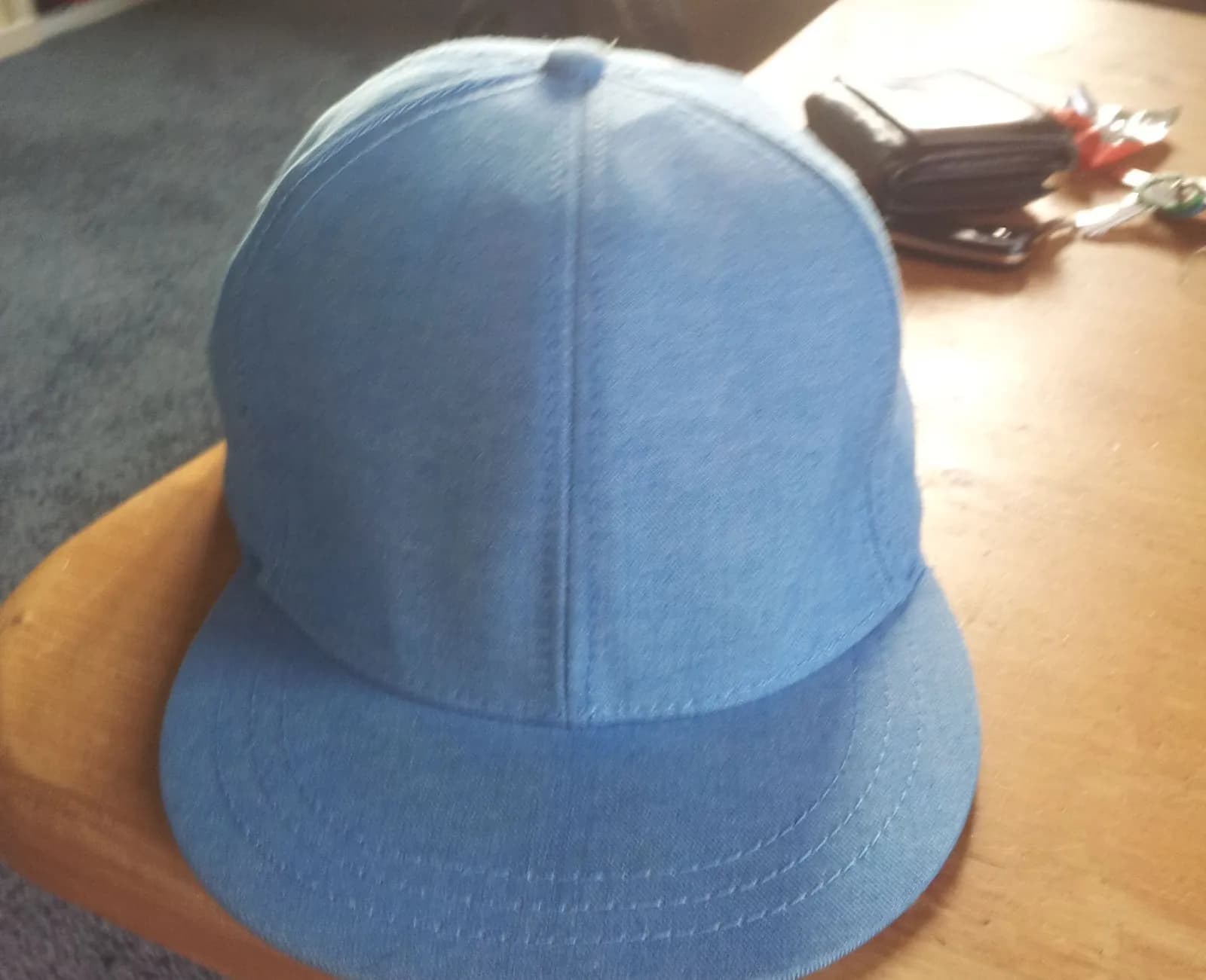 Casquette en toile bleu clair posée sur le coin d'une table en bois, un portefeuille et des clés en arrière-plan