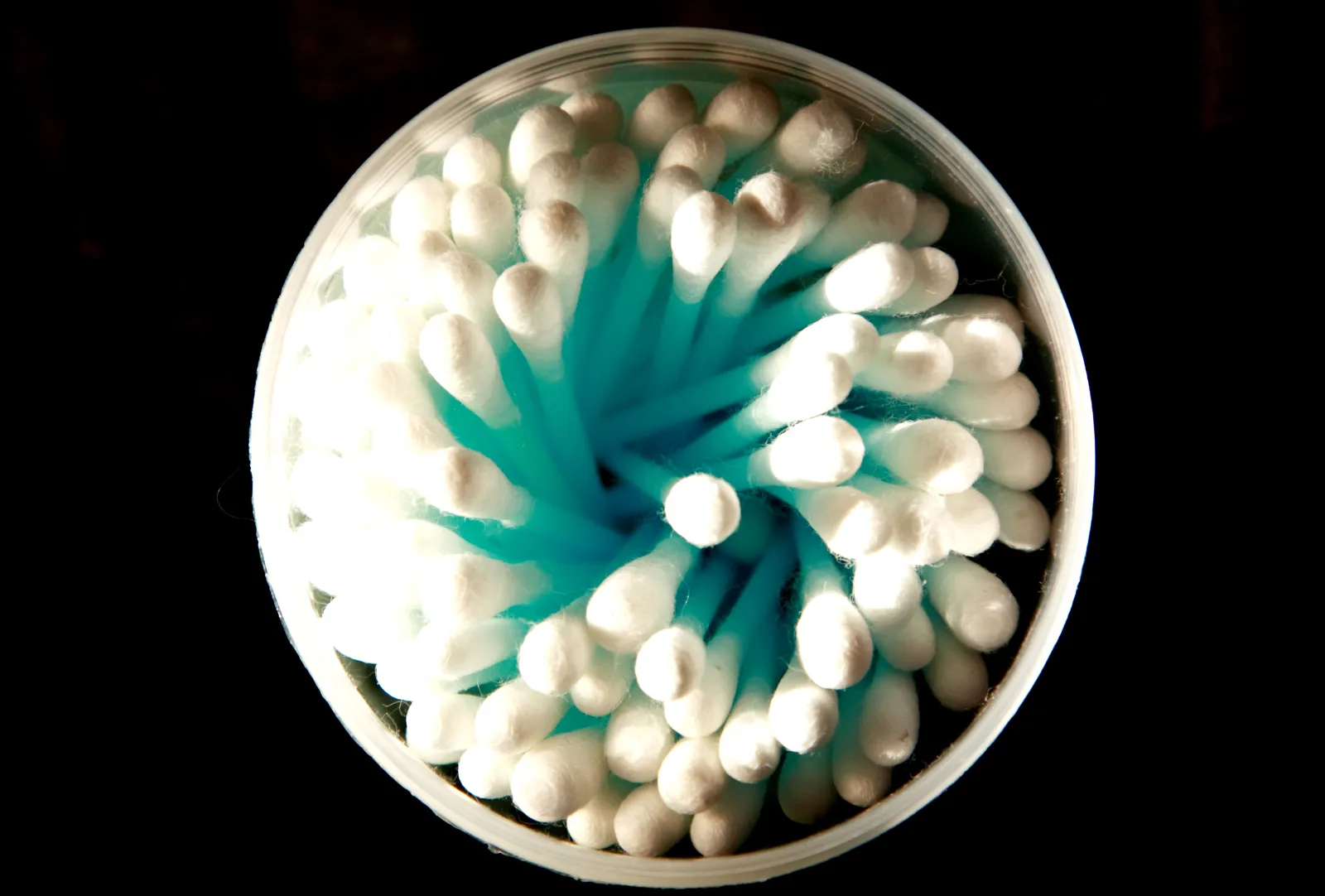 Cotons-tiges blancs rangés en spirale dans une boîte ronde transparente, vus du dessus sur fond noir
