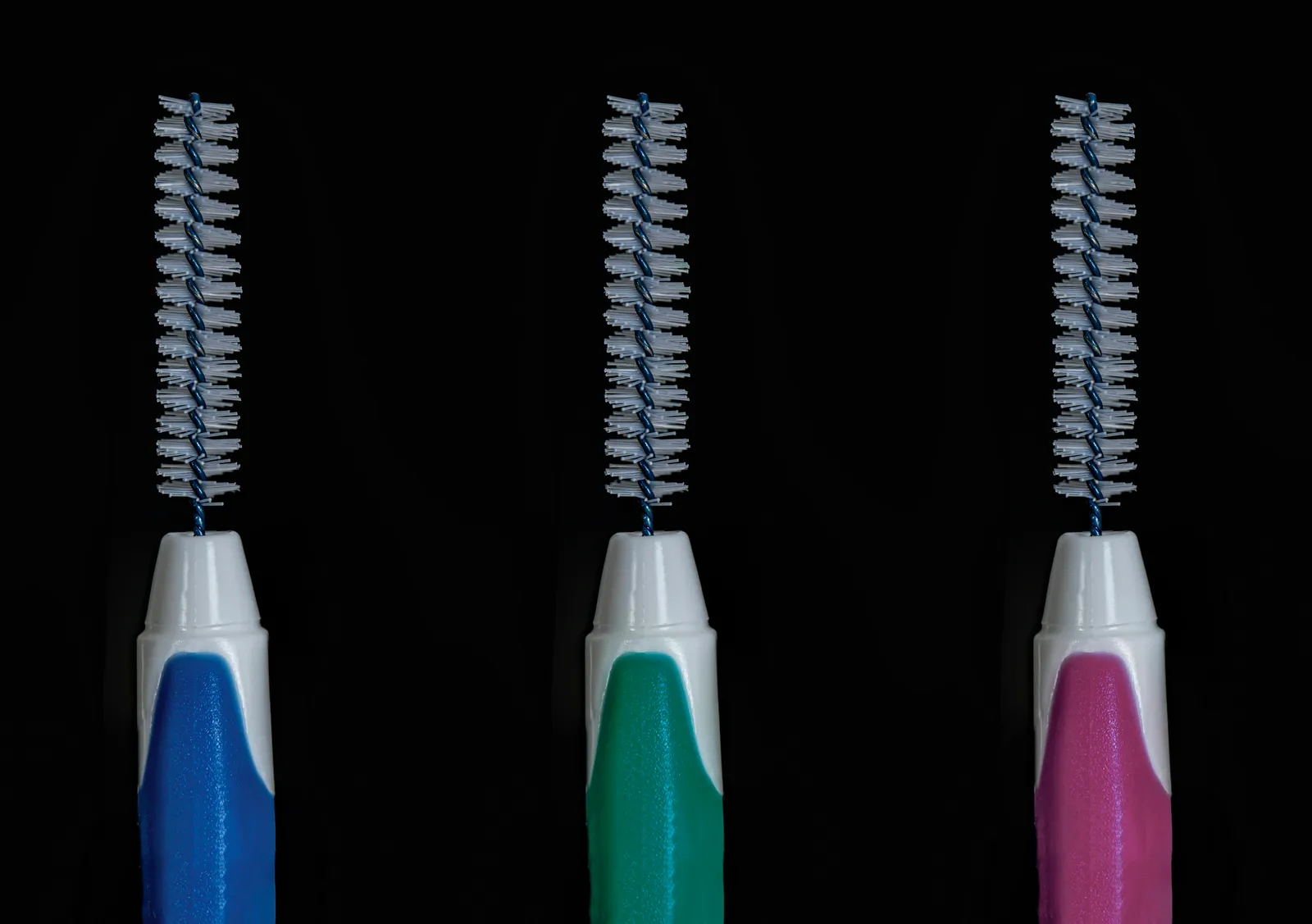Trois brossettes interdentaires de couleurs différentes sur fond noir