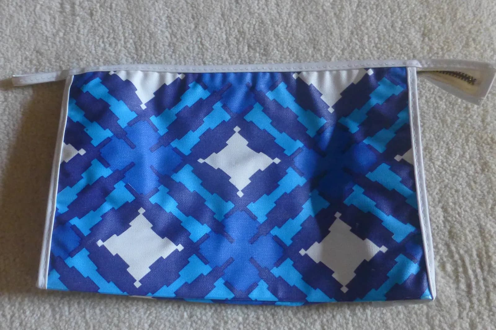 Trousse de toilette zippée à motifs bleus et blancs posée à plat sur un tapis beige