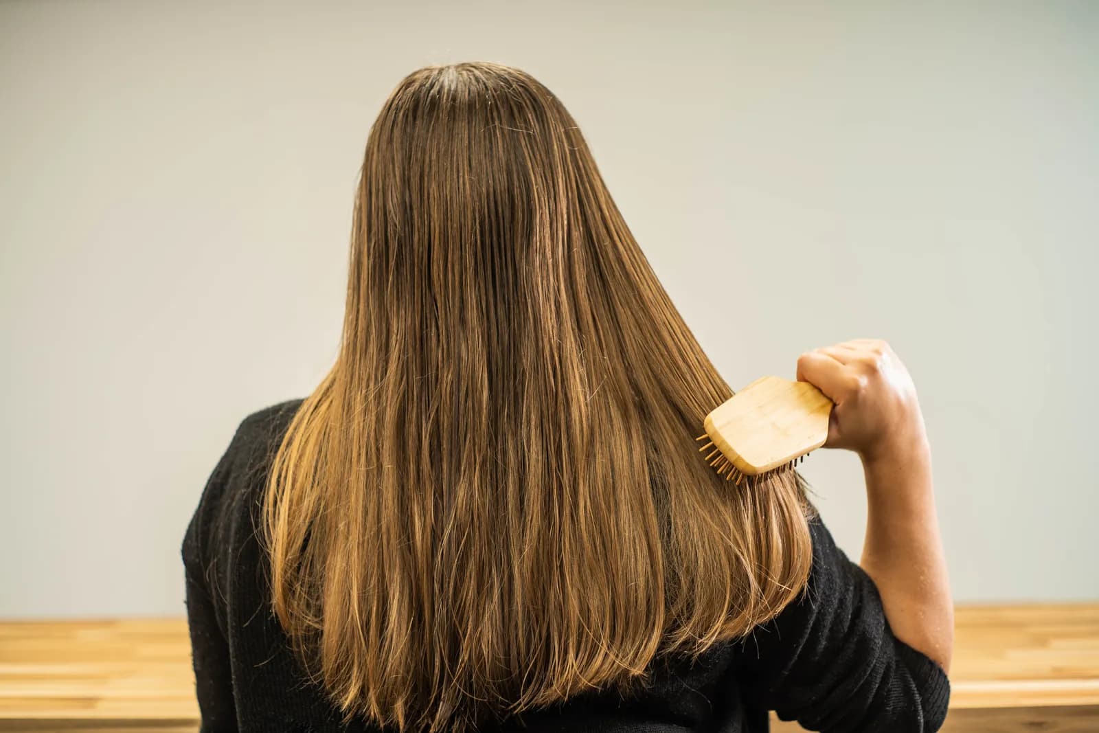 Femme vue de dos, aux longs cheveux châtains encore humides, qui se brosse avec une brosse en bois