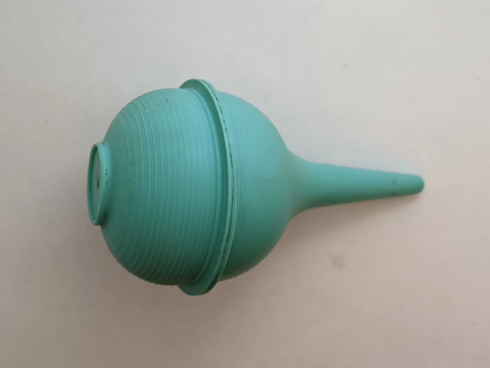 Poire en caoutchouc vert d'eau à embout fin, posée sur une surface claire