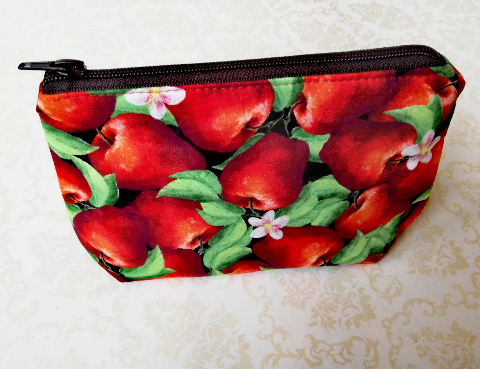 Petite trousse en tissu à fermeture éclair, imprimée de pommes rouges, posée sur une nappe claire