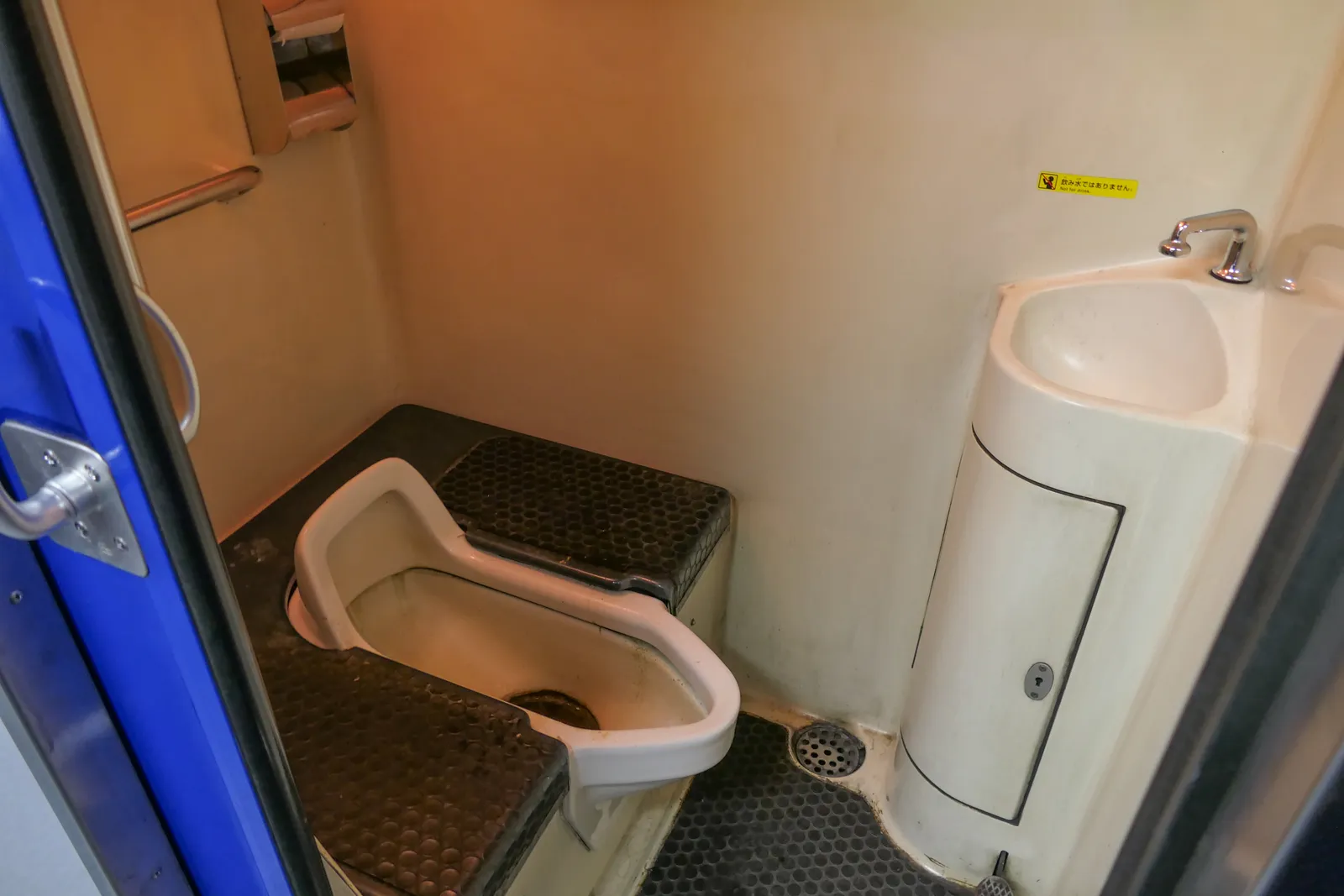 Toilettes d'un train : cuvette à la turque, petit lavabo arrondi et barre d'appui dans une cabine étroite