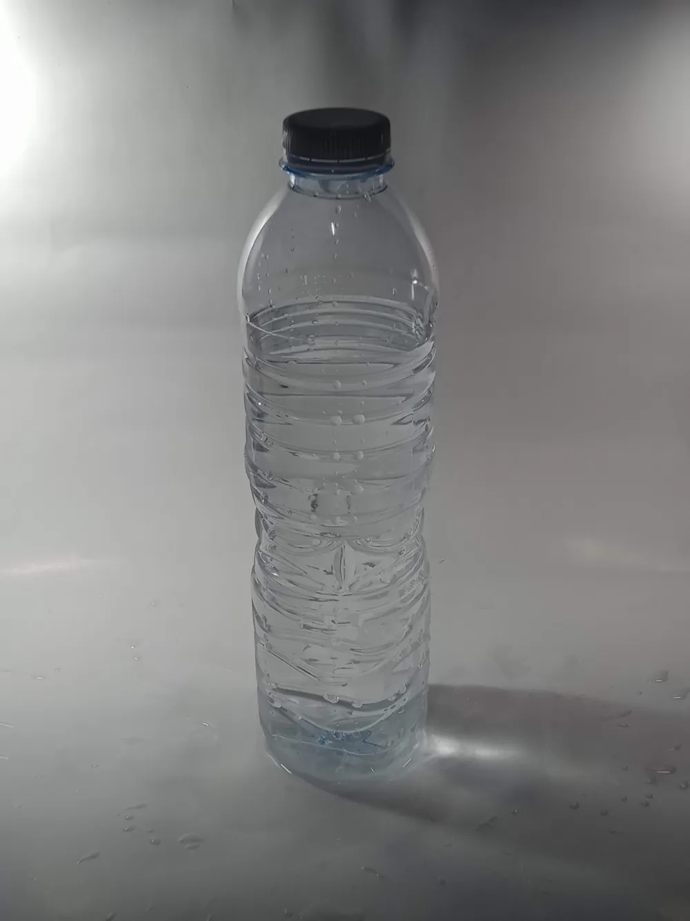 Bouteille d'eau en plastique transparent, bouchon fermé, posée sur un fond gris clair