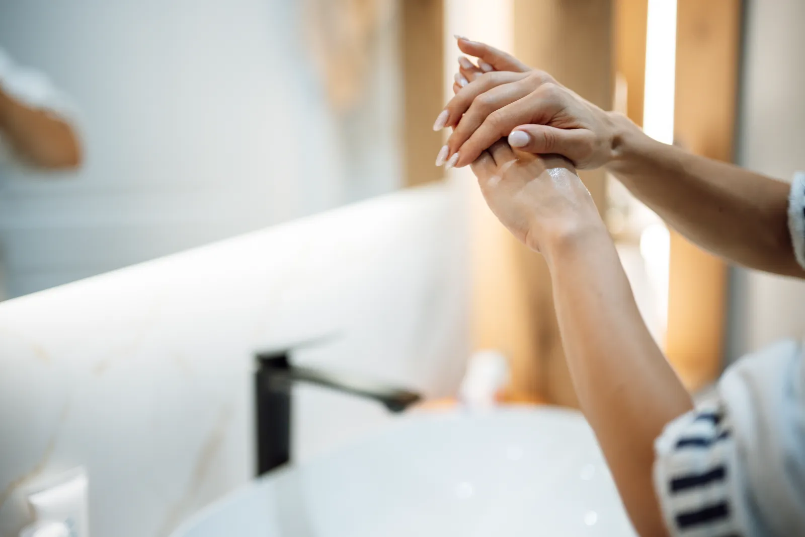 Mains savonnées au-dessus d'un lavabo blanc, dans une salle de bain claire, avant un soin