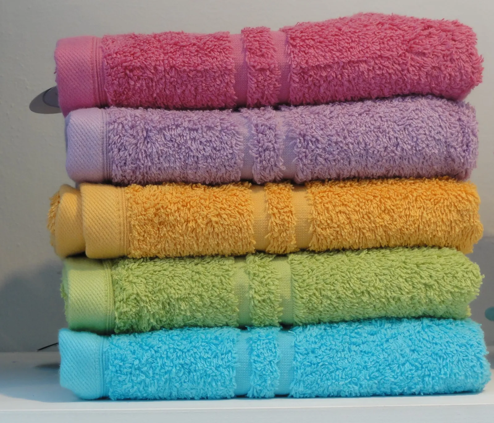 Pile de serviettes de toilette pliées, rose, mauve, orange, vert et bleu, posée sur une étagère blanche