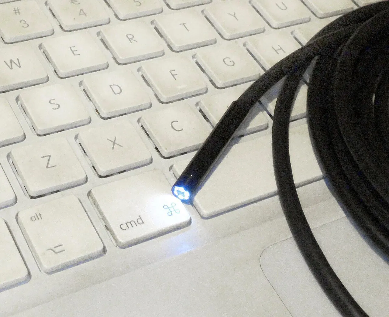 Extrémité éclairée d'une caméra d'inspection miniature au bout d'un câble noir, posée sur un clavier d'ordinateur