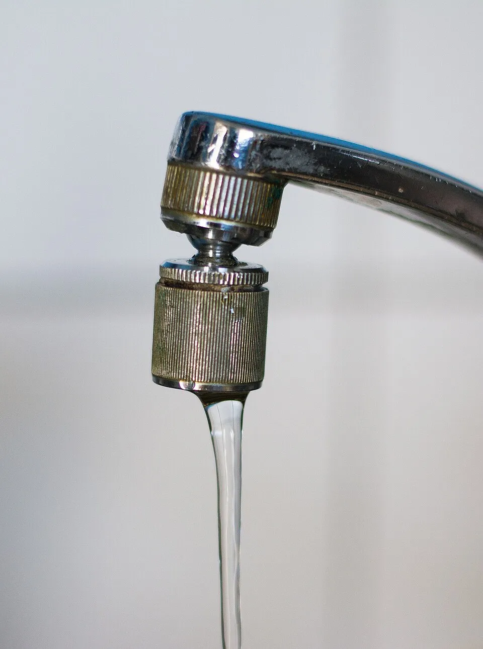 Filet d'eau qui s'écoule d'un robinet chromé, devant un mur clair