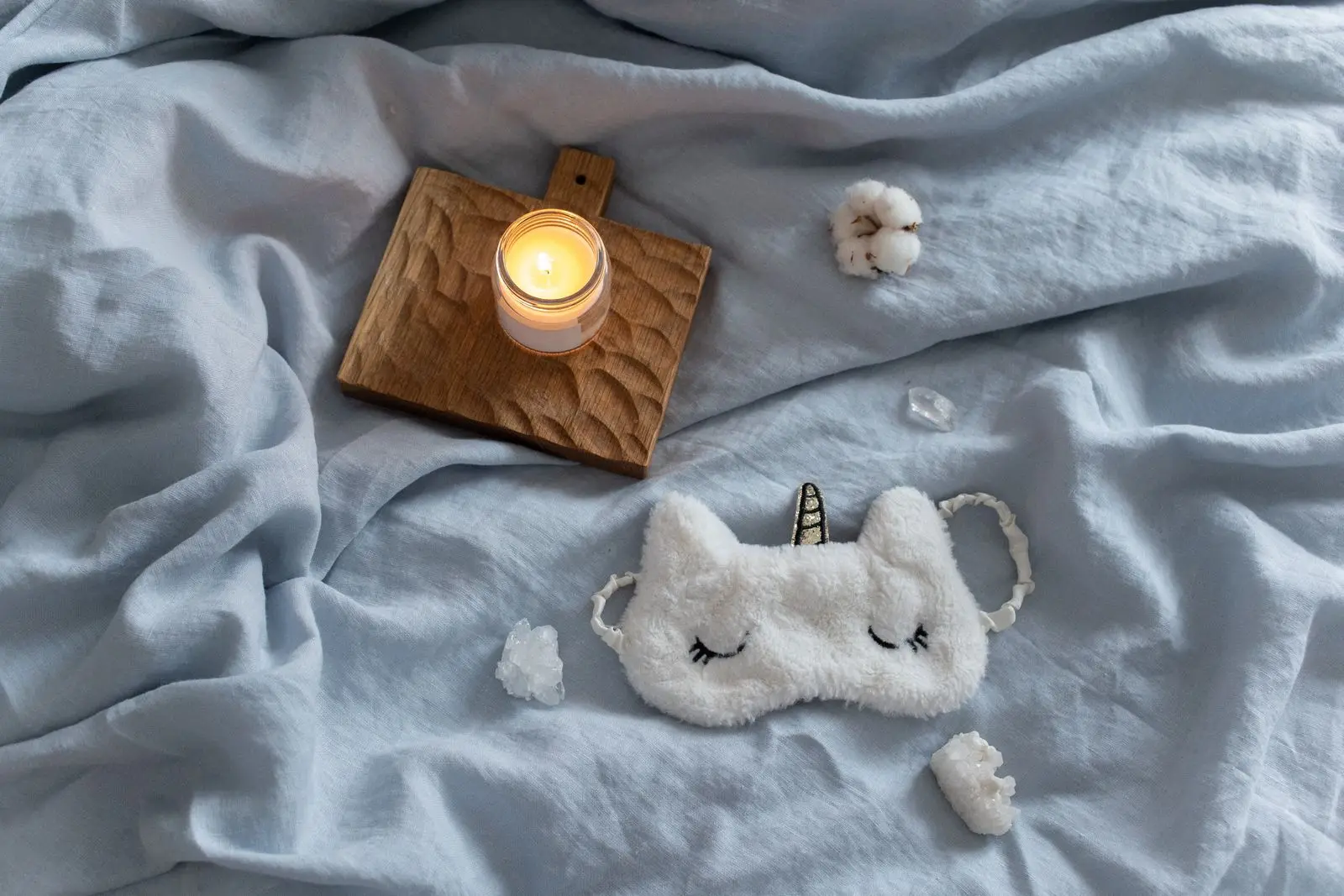 Bougie allumée et masque de nuit posés sur un lit, ambiance douce du soir avant de dormir